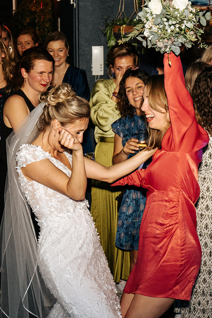 Bruid en vrouw in rode jurk dansen vrolijk samen op een feest.