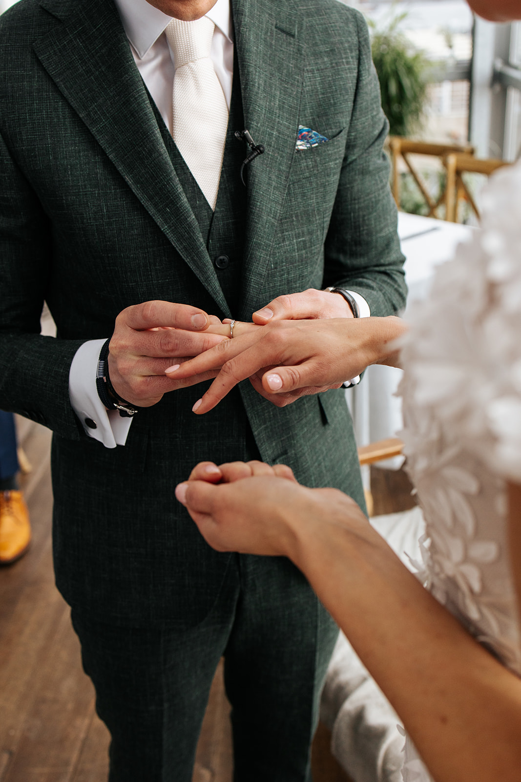 Man in groen pak schuift een ring aan de vinger van een vrouw in trouwjurk.
